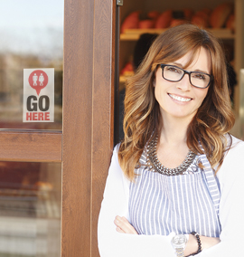 Woman standing inside doorway of business that has a "Go Here" sign in the window